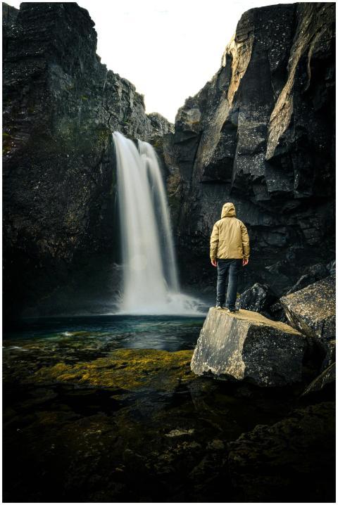 A man stands on rocks, exploring a breathtaking wa