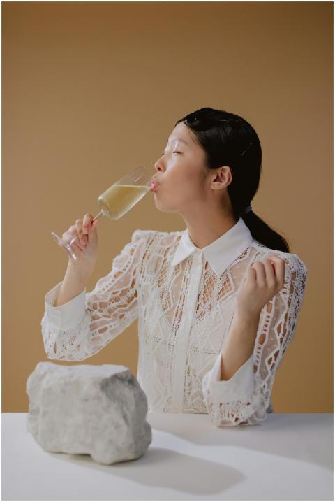 A woman in a lace dress savoring a drink with eyes