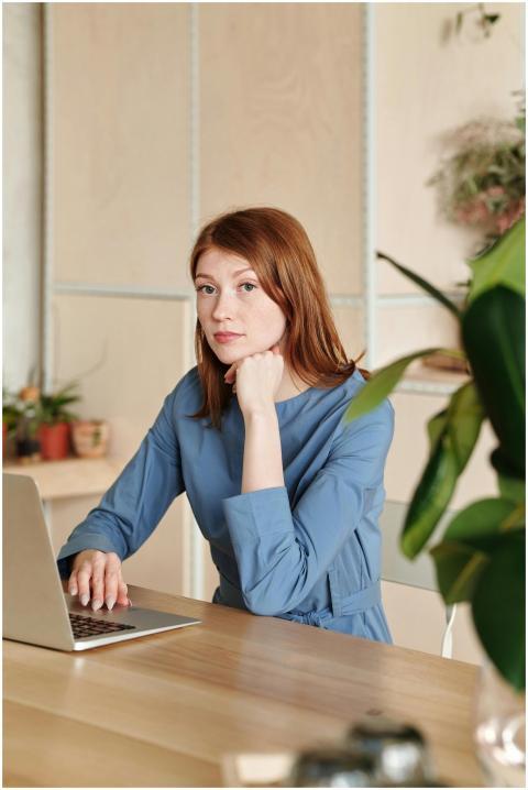 Caucasian woman in blue dress working on a laptop