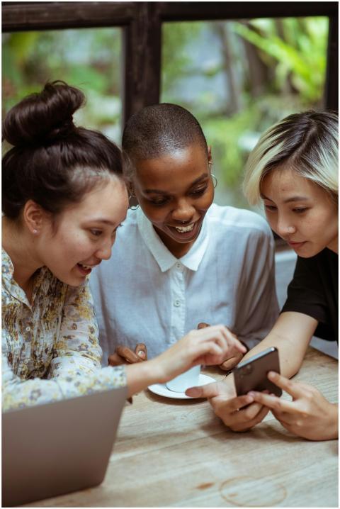 Three diverse women smile while using a smartphone