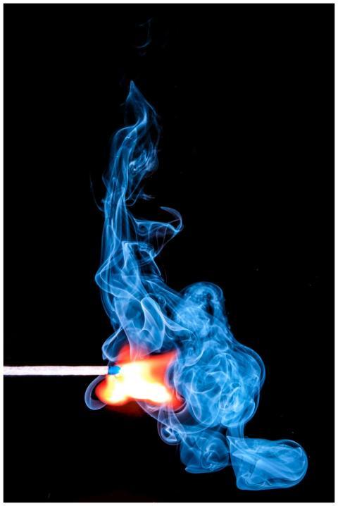 A match ignites with vibrant blue smoke against a