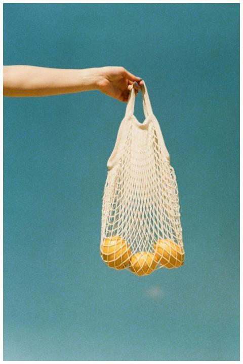 A hand holds yellow lemons in a reusable net bag a