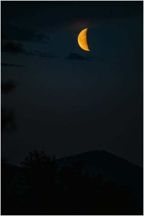 A serene crescent moon in a deep night sky above t