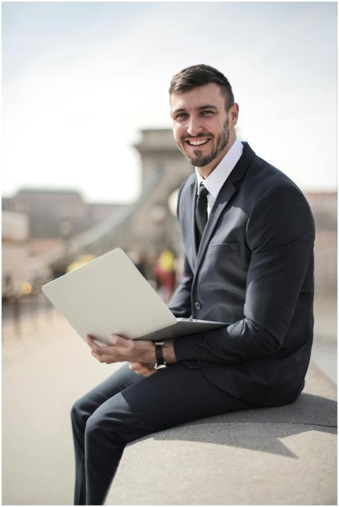 Happy businessman in suit holding laptop while sit