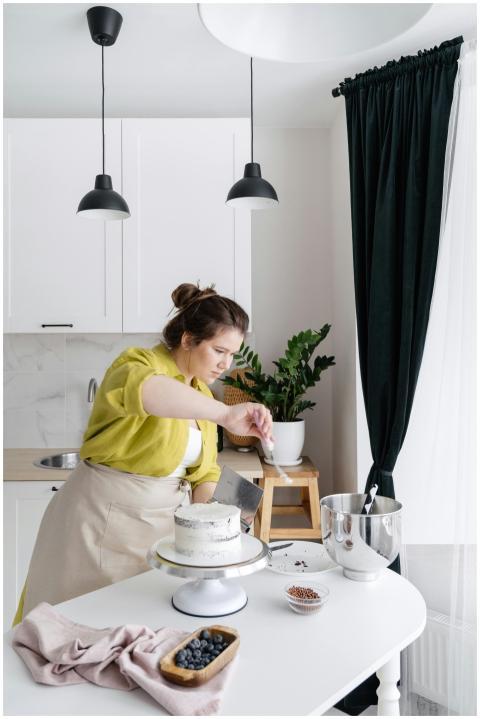 A woman in an apron decorates a cake in a bright,