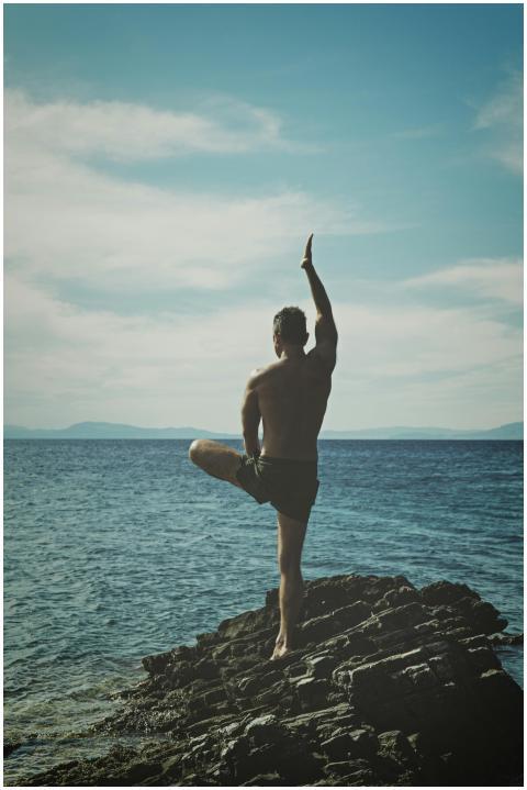 Back view of a man practicing yoga on a rocky seas