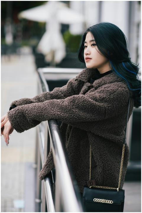 Asian woman in fashionable outfit leaning on raili