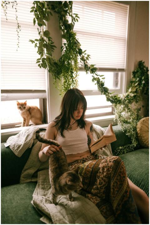 A woman reading on a sofa with cats and lush indoo