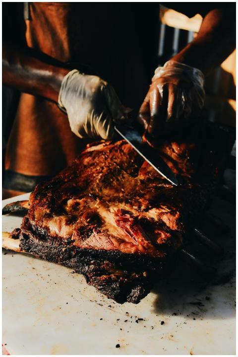 A skilled chef slices roasted steak on a barbecue