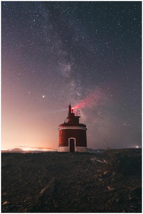 Tranquil scene of a red lighthouse under a starry
