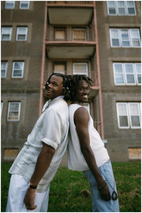 Two young men stand back to back, smiling outside