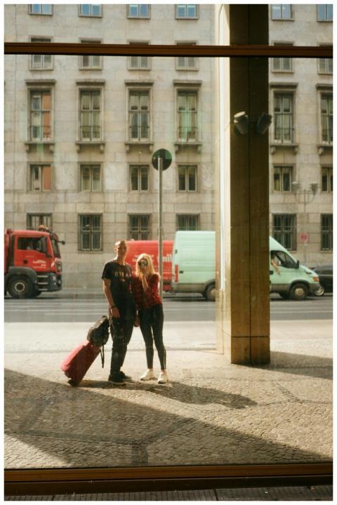 A young couple with luggage stands on a city sidew