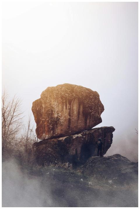 A lone hiker stands by large rock formations in a