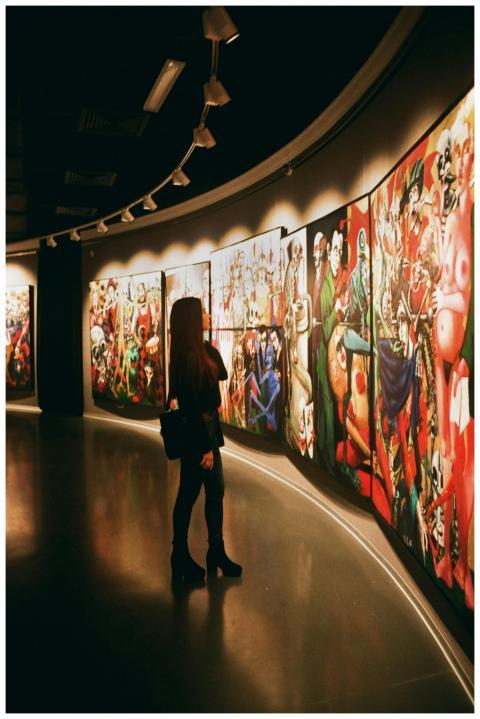 A woman observes vibrant paintings in an art galle