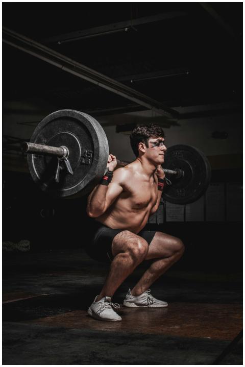 Shirtless man performing a barbell squat, showcasi