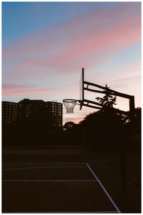A silhouette of a basketball hoop against a vibran