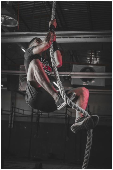 A determined man climbing a rope in an indoor gym