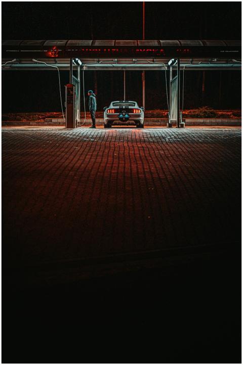 A man stands next to a car at a gas station at nig