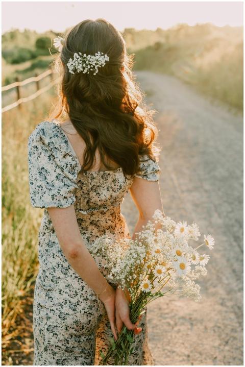 A woman holding a bouquet of daisies on a sunlit p