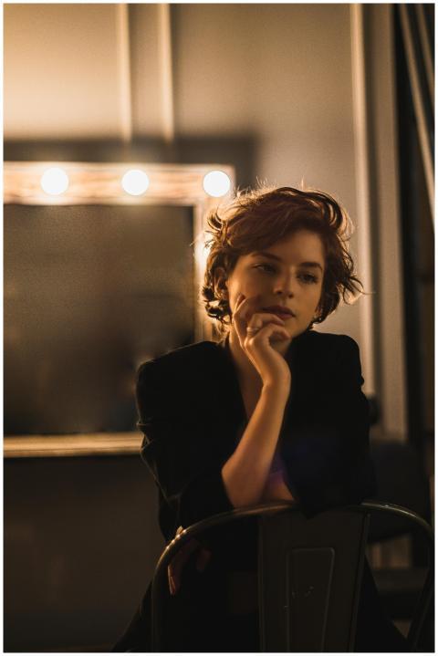 A woman with short hair sits pensively in a dimly