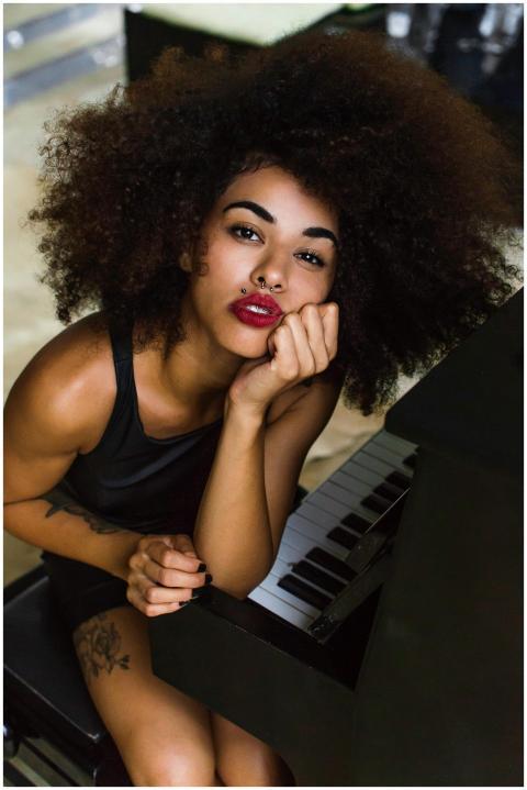A beautiful woman with curly hair poses at a piano