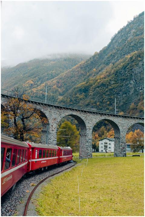 Red train passing under stone arches in a mountain