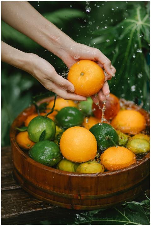Hands washing fresh citrus fruits in a wooden bowl