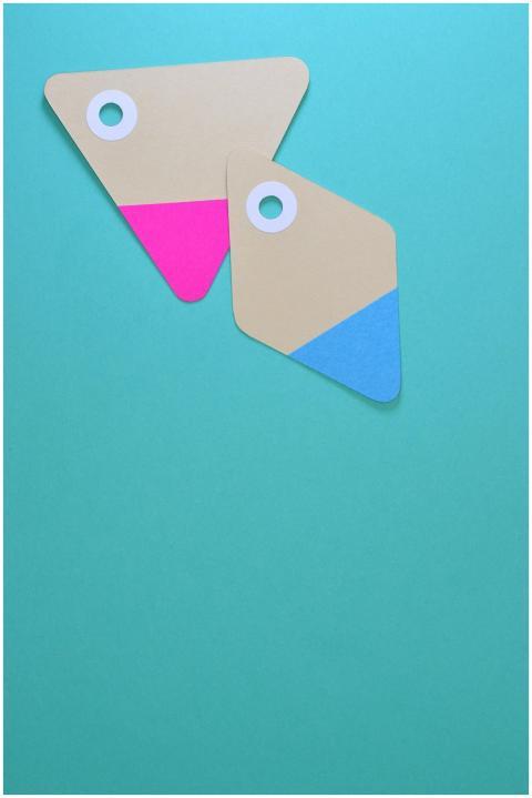 Two colorful paper tags with holes on a teal backg