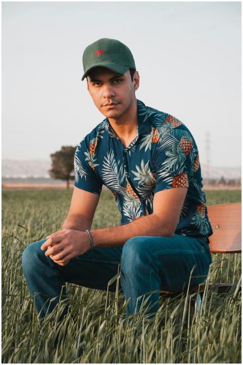 Young man in Hawaiian shirt and cap sitting on a c