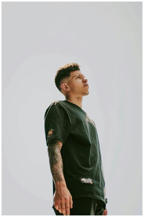 A young man with tattoos stands confidently outdoo