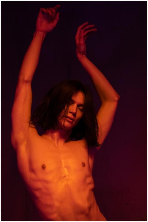 A shirtless male dancer with long hair posed expre