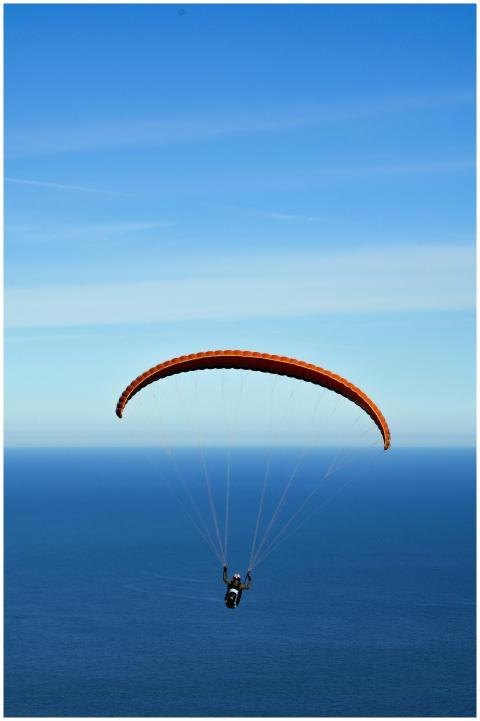 A person paragliding with an orange chute over a v