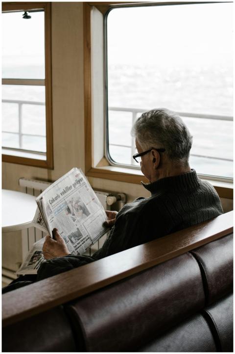 Elderly man reading newspaper inside ferry, enjoyi