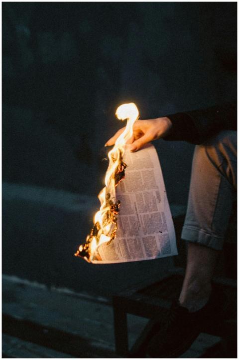 A close-up view of a newspaper set ablaze, held by