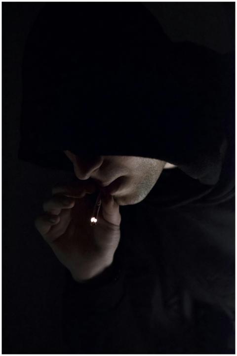 A mysterious individual in a hoodie smoking in the