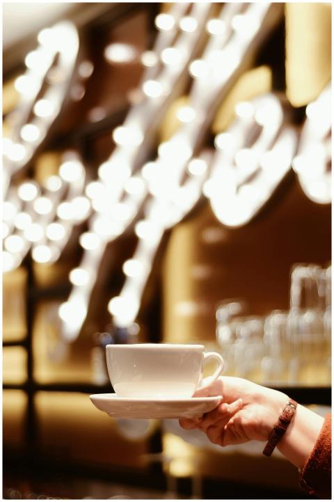 Hand holding a coffee cup indoors with blurred sty