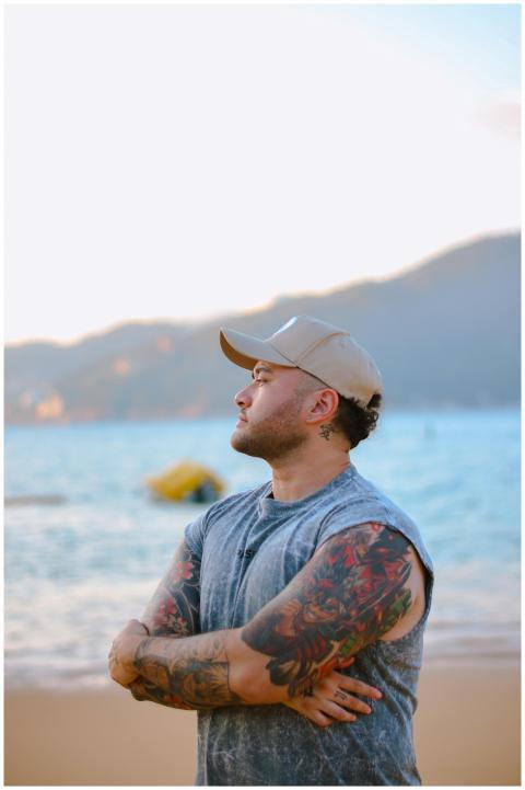 Man with tattoos gazing at scenic beach sunset, ar