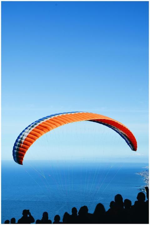 Silhouette of people watching paraglider soar over