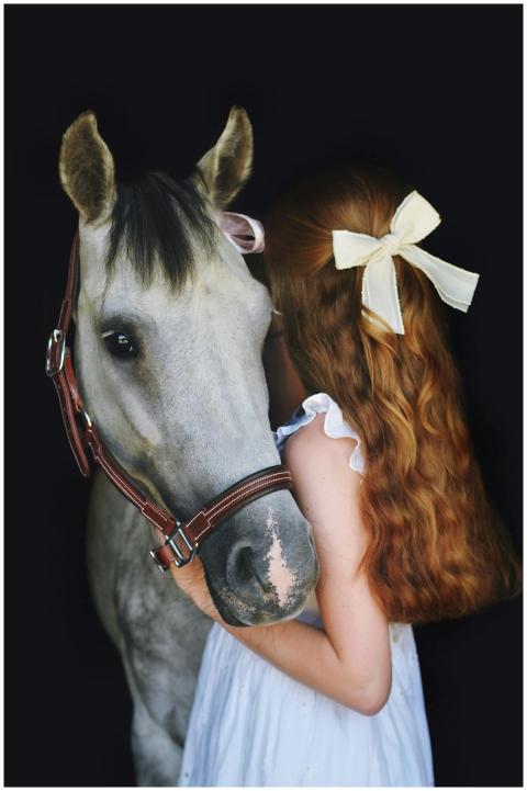 Young girl with red hair and bow embraces a white