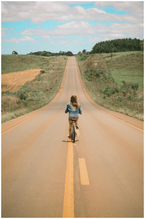 A blonde girl rides a bicycle down a long scenic h