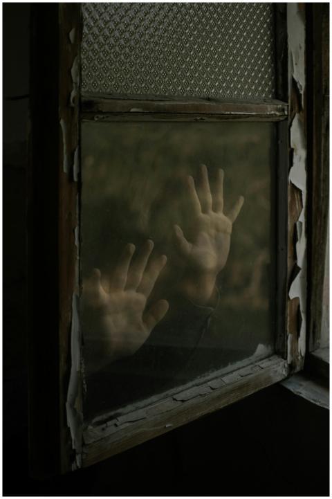 Mysterious hands pressed against an aged window, e
