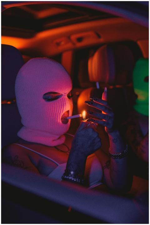 Two masked individuals in a car under neon lightin