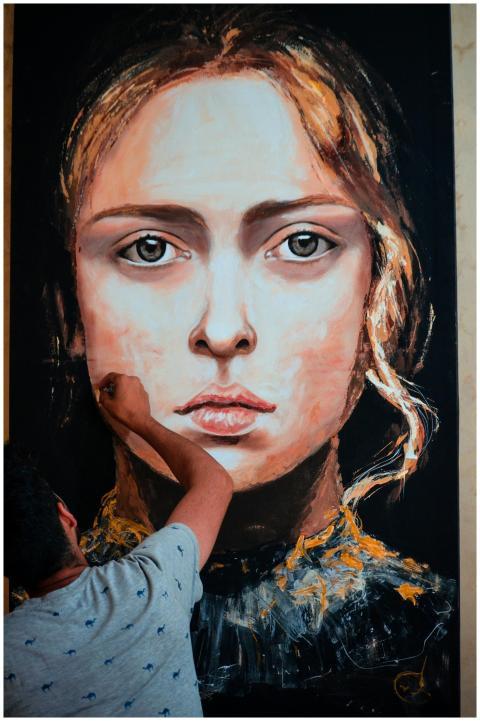 An artist meticulously paints a large portrait of