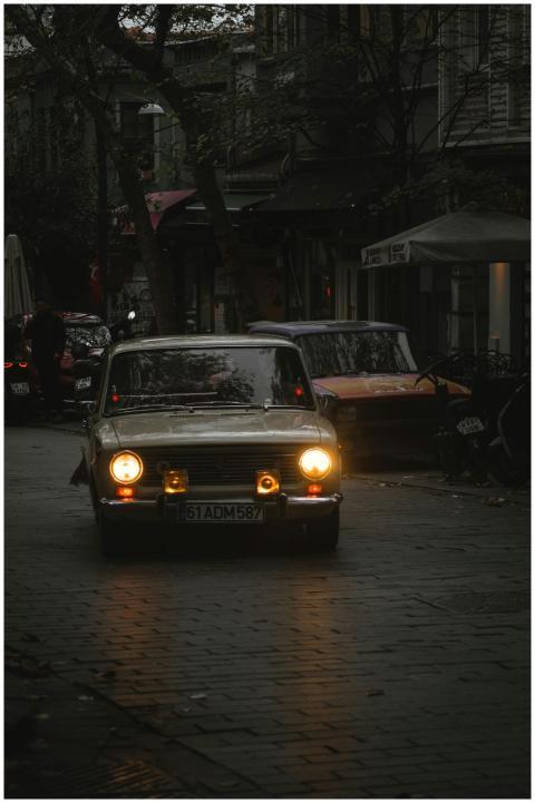 A vintage car drives on a rainy, dimly lit street