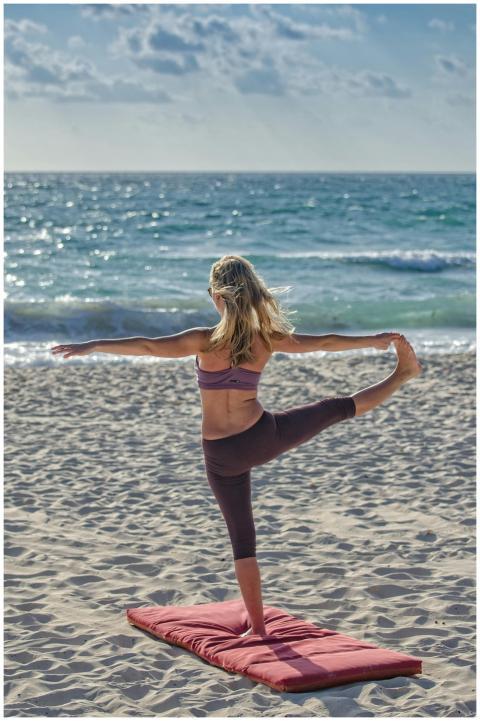 A woman performs yoga on a sandy beach at sunrise,