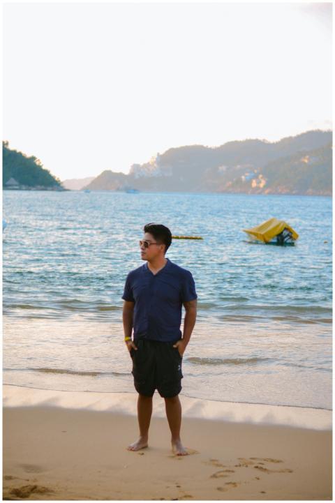 A man stands on a sandy beach with scenic ocean an