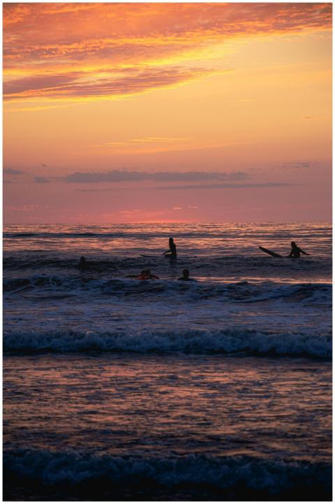 Silhouetted surfers ride the waves as the sun sets