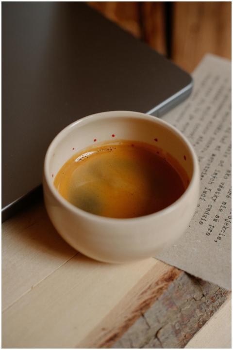 Warm espresso in a ceramic cup next to a laptop on