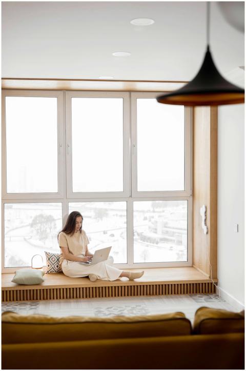 Young woman sitting by a large window, working on