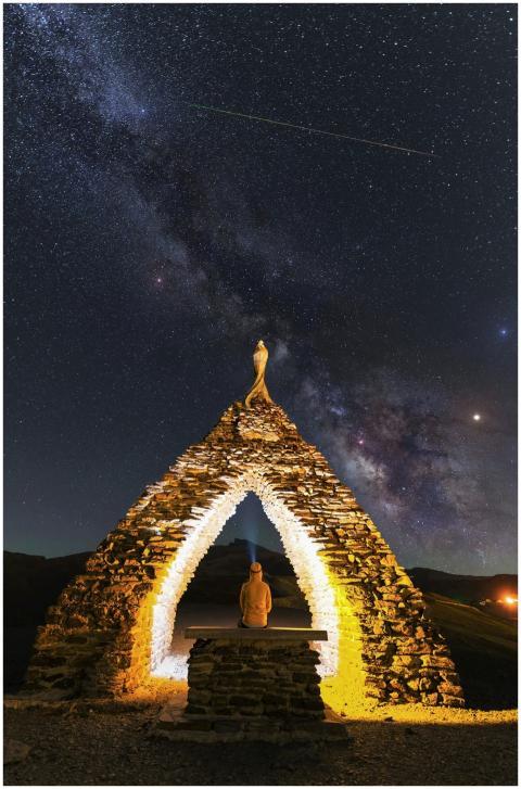 A person sits under an illuminated stone arch with